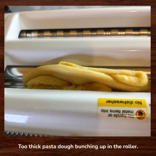 Pasta dough that is too thick bunching up and folding inside a pasta roller instead of feeding through smoothly on the first pass.