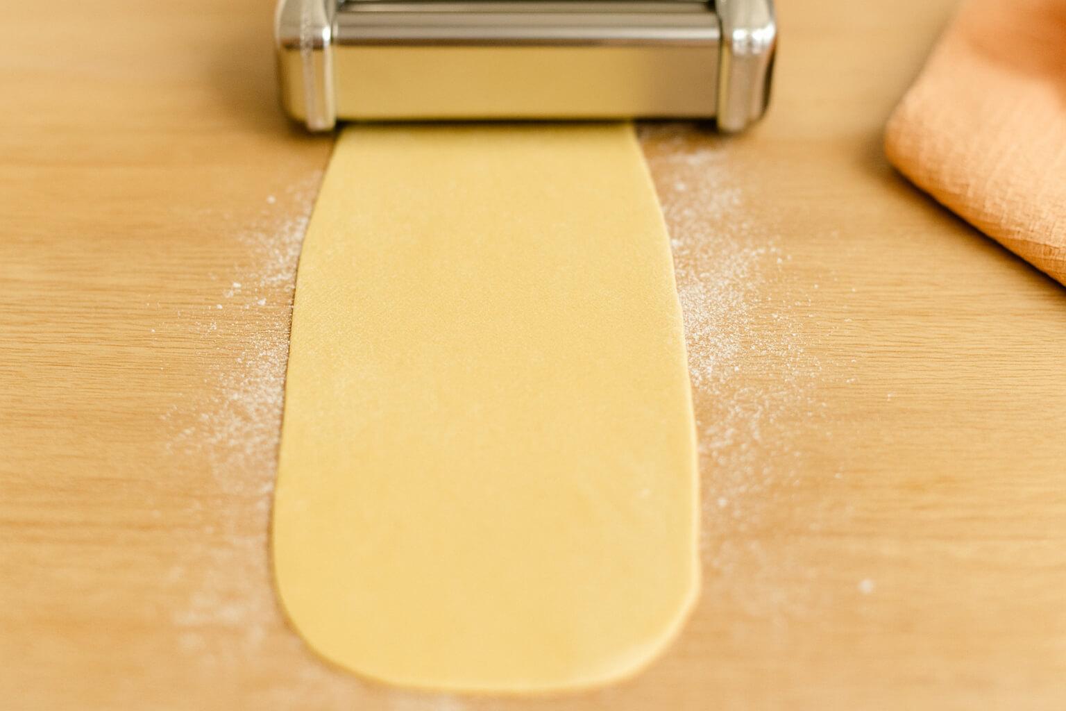 Smooth pasta sheet resting on a lightly floured board with a pasta cutter nearby, showing how to let dough dry briefly before cutting.